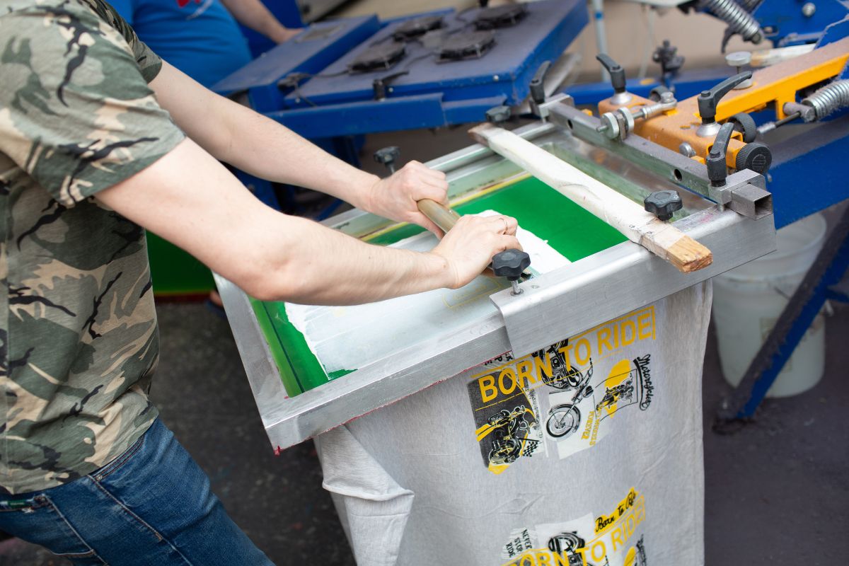 A man is printing designs into T shirts utilizing various types of shirt printing techniques