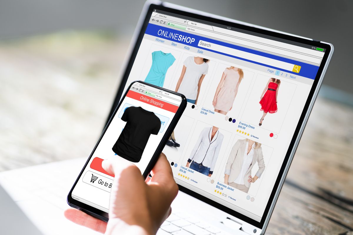Person buying custom t shirt online using phone alongside laptop