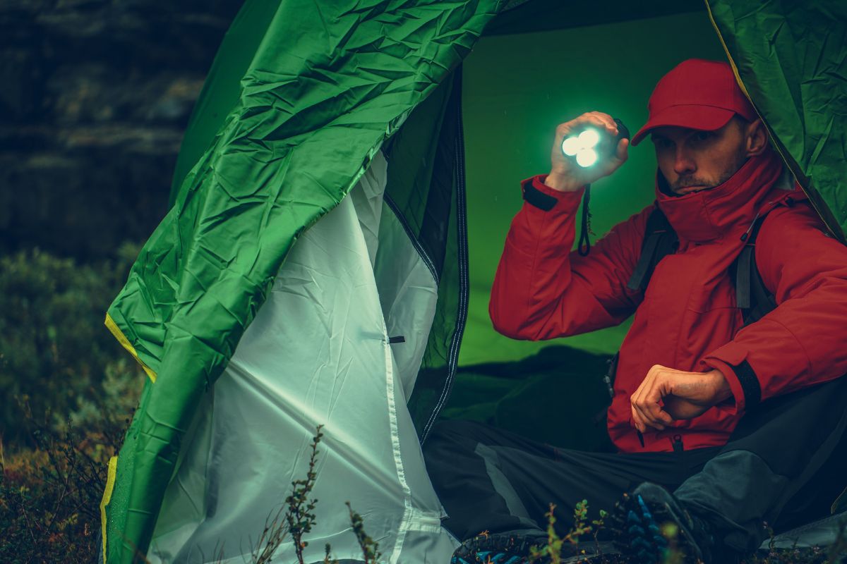 A man camping outdoors and using a flashlight