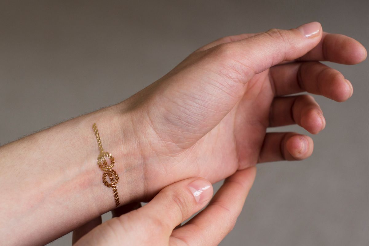 A women with a gold metallic custom tattoo on her hand made by swagify